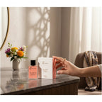fragume Bloom Spirit Eau De Parfum bottle and box on a marble vanity with a floral bouquet in the background